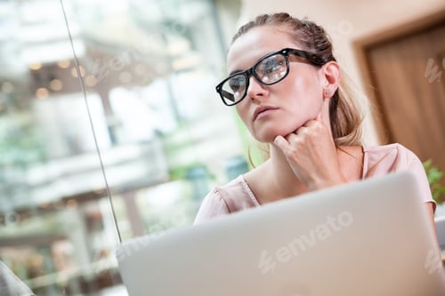Preview: Business woman working with laptop and thinking about future at open space office in modern interior