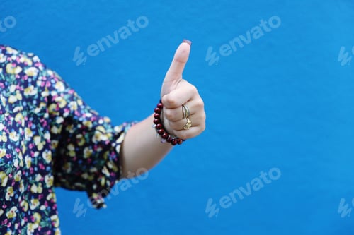 Preview: A young lady showing thumbs up against a blue wall