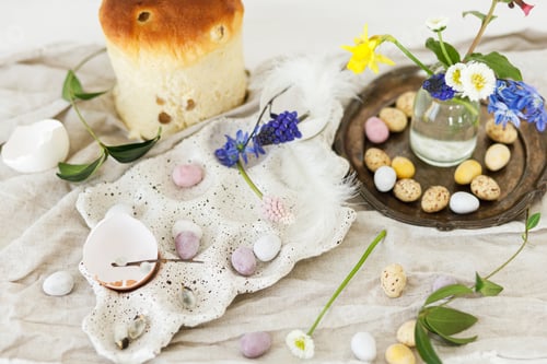Preview: Colorful easter chocolate eggs, easter bread, spring flowers and linen cloth on rustic wooden table
