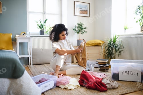Preview: Young woman sorting wardrobe indoors at home, charity donation concept.