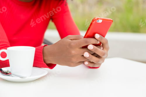 Preview: Cropped photo of the hands of a woman using mobile with cup of coffee outdoors