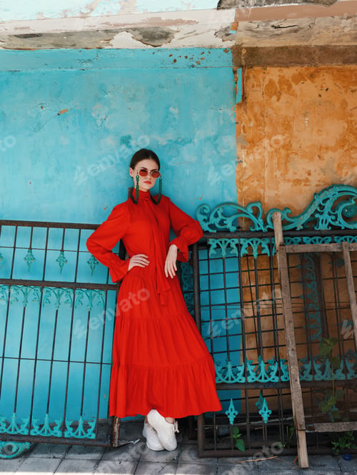 Preview: Elegant woman in vibrant red dress poses against striking blue and yellow backdrop