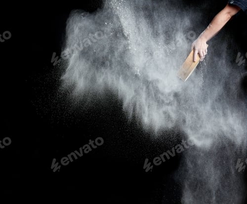 Preview: Female hand sifts white wheat flour through a round wooden sieve on a black background