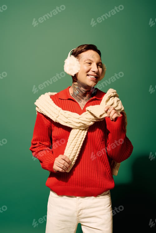 Preview: A cheerful young man with tattoos in a cozy sweater posing playfully against a green backdrop