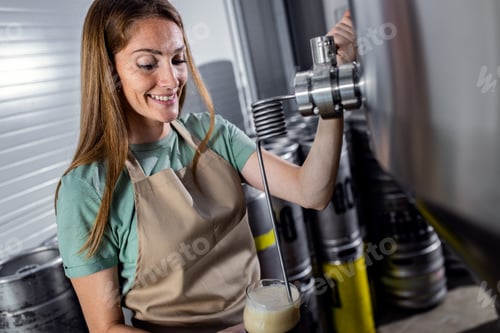 Preview: Female brewer working in craft brewery examining quality of the beer.