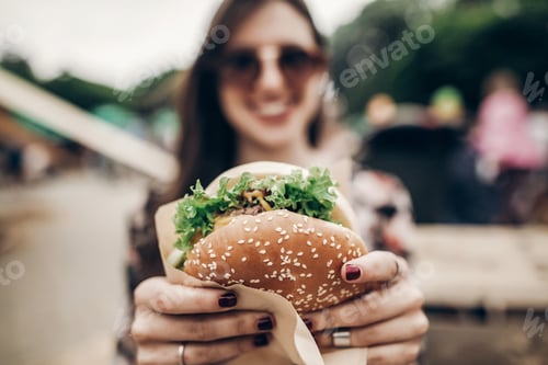 Preview: Stylish hipster woman holding juicy hamburger in hands close up