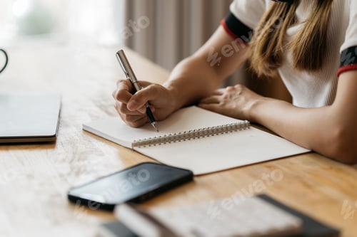 Preview: Close up of student girl hand writing on notebook on a desk at home.