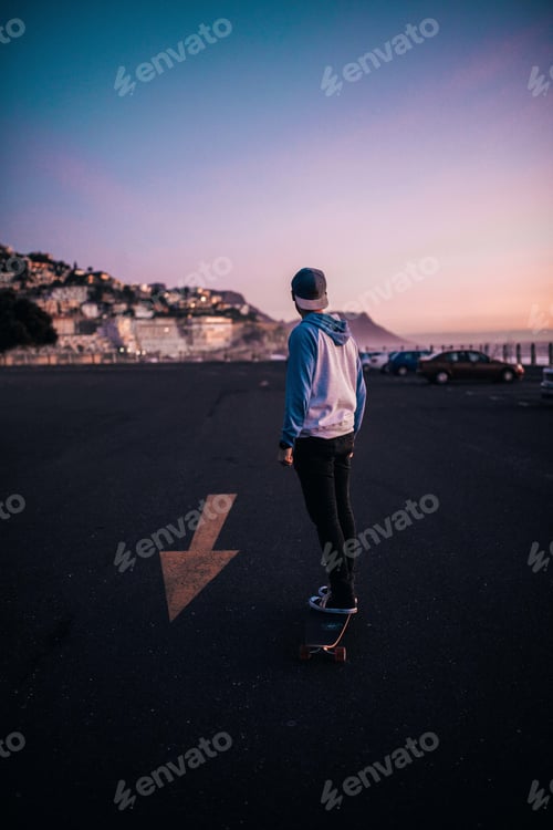 Preview: Hipster guy longboarding on parking lot at sunset