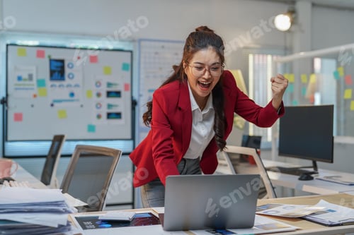 Preview: Enthusiastic businesswoman in a red blazer is celebrating a successful business achievement while wo