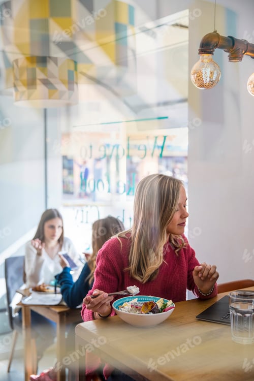 Preview: Woman eating muesli in cafe, using laptop