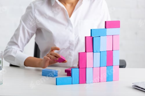 Preview: Cropped view of businesswoman stacking building blocks at working table