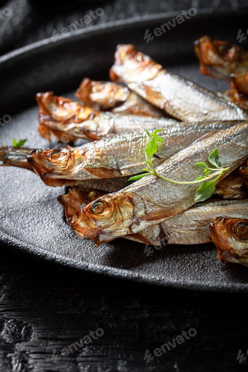 Preview: Salty smoked sprats on a black plate and burnt table.