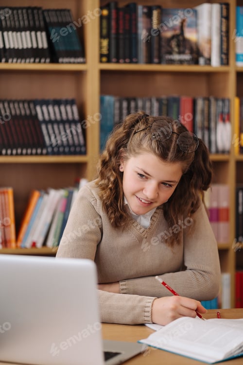 Preview: Girl studying among books using laptop