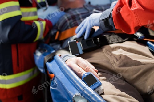 Preview: Cropped view of patient with heart rate monitor lying on stretcher near paramedics
