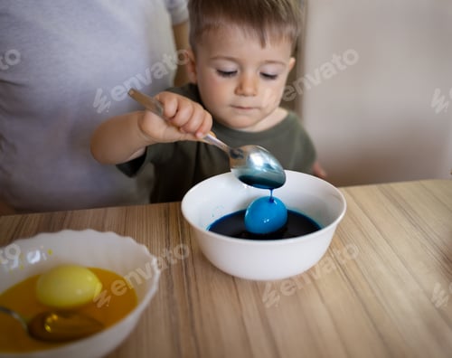Preview: little cute boy paints eggs for easter sitting in the kitchen at the table