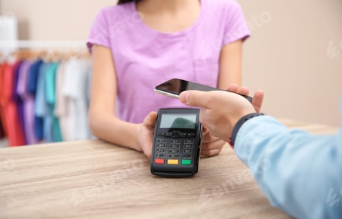 Preview: Man using terminal for contactless payment with smartphone in shop, closeup