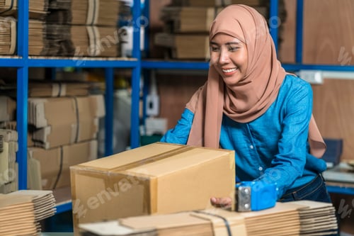 Preview: Warehouse Muslim worker woman packing cardboard box with sticky tape in local warehouse