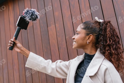 Preview: Young latin woman recording video content with mobile phone and microphone