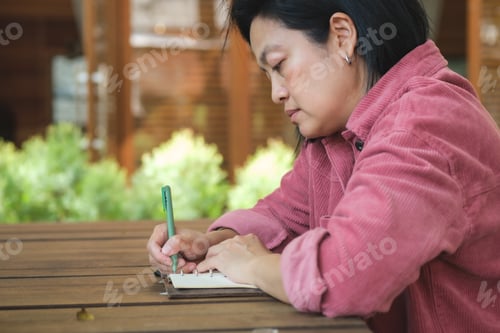 Preview: woman writing goal on notebook at coffee shop outdoor space