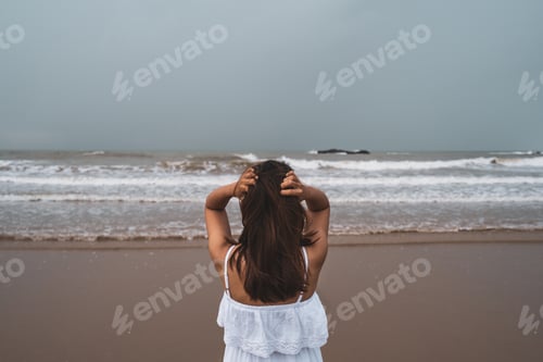 Preview: Young woman feeling lonely and sad looking at the sea on a gloomy day