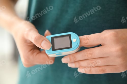 Preview: Young woman checking pulse with blood pressure monitor on finger, closeup