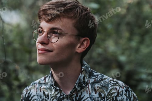Preview: Portrait of a young Caucasian male with eyeglasses looking aside in a garden