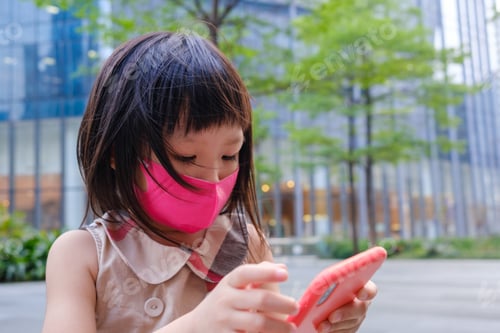 Preview: Asian child wearing mask and using cell phone in city