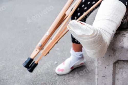 Preview: unrecognizable girl sits on the street on a bench with a broken leg and crutches.disabled girl with