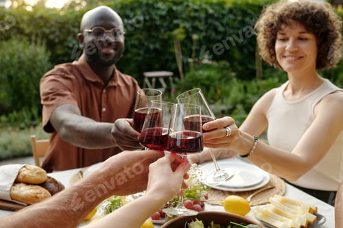 Preview: Focus on hands of four adults clinking with red wine over served table