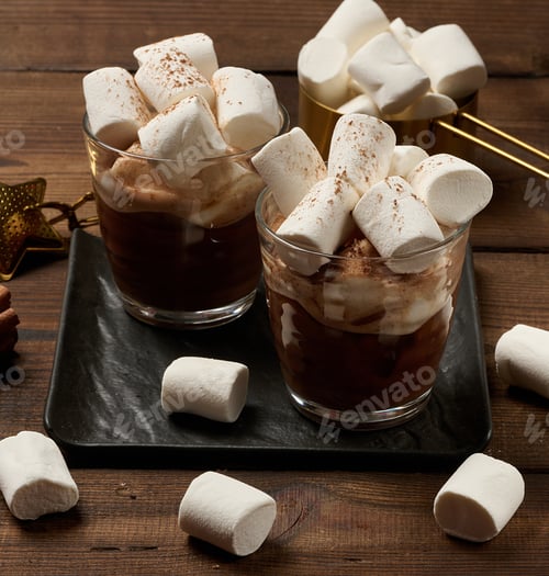 Preview: Two glasses of hot chocolate with fluffy marshmallows on a slate board.