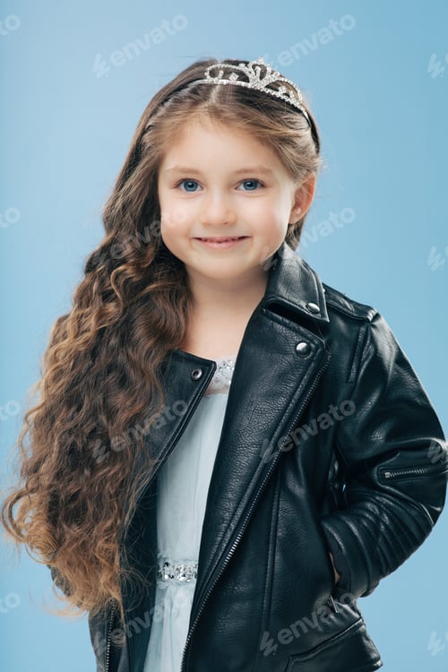 Preview: Vertical shot of attractive small female child has long curly hair, wears crown and leather jacket