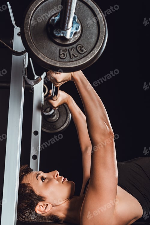 Preview: attractive young sportswoman exercising with barbell, black background