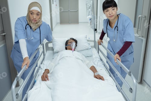 Preview: Diverse female doctors pushing emergency stretcher bed with mixed-race female patient in corridor