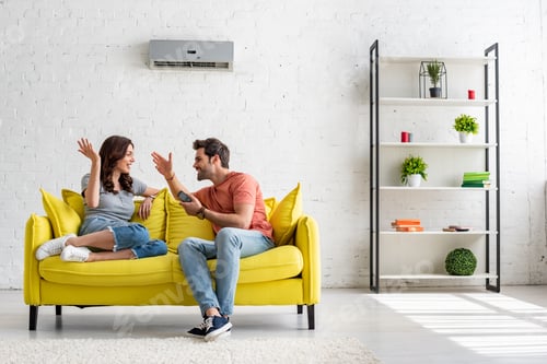 Preview: Couple Laughing Together on Yellow Couch Indoors