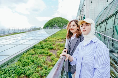 Preview: Two young women on green urban rooftop looking into distance