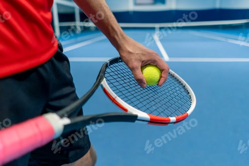 Preview: close-up of a hand holding a tennis ball and racket on an indoor tennis court preparing to serve