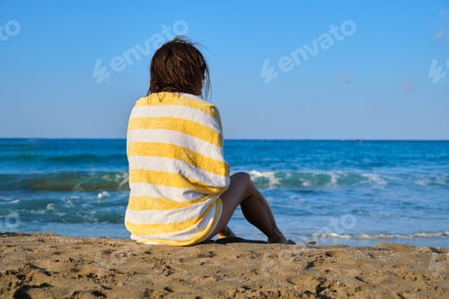 Preview: Mature beautiful woman with beach towel sitting on sand, woman enjoying sea sunset landscape