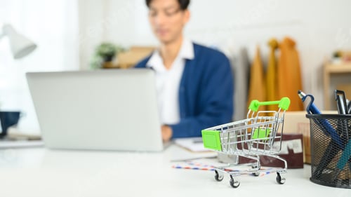 Preview: Small shopping cart on desk with entrepreneur working in background.