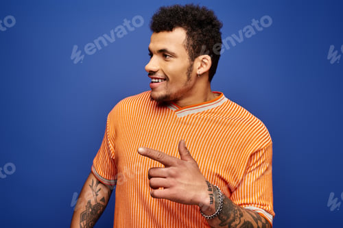 Preview: Handsome man in an orange striped shirt smiling and pointing against a blue background