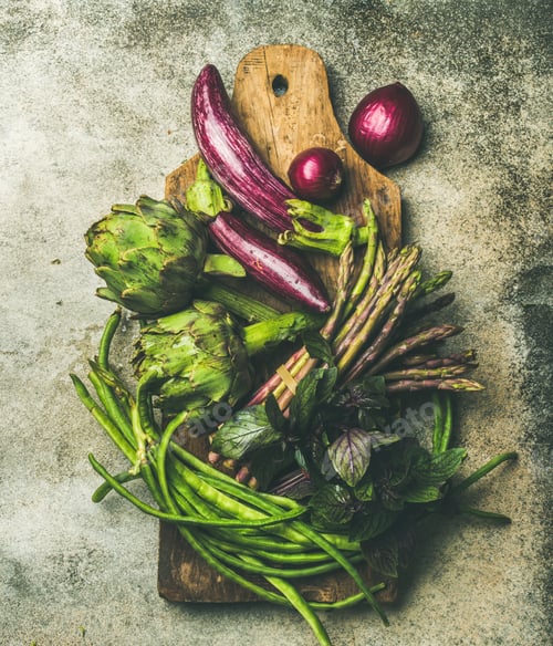 Preview: Flat-lay of green and purple vegetables on board, grey background