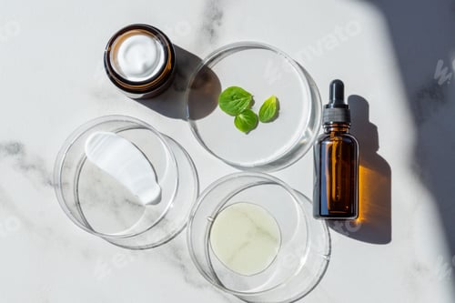 Preview: Glass petri dish with yellow pure serum for skin care and cream swatch on white marble background,