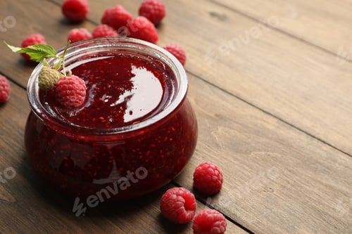 Preview: Tasty raspberry jam in glass jar on wooden table, closeup. Space for text