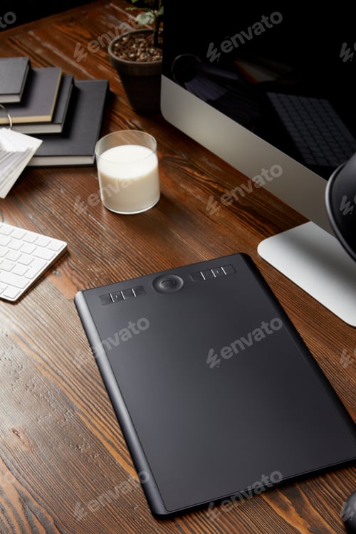 Preview: close up view of graphic designer workplace with graphic tablet, glass of milk and notebooks on