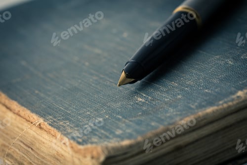Preview: Old book with a pen resting on its cover at a quiet workspace during the day