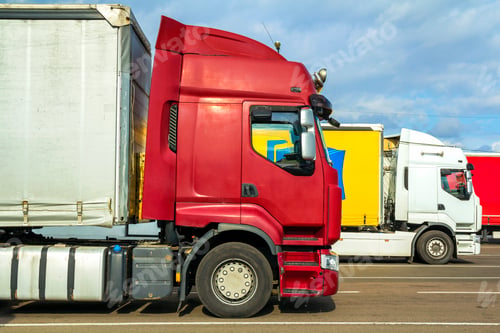 Preview: Colorful modern big semi-trucks and trailers of different makes and models stand in row on flat