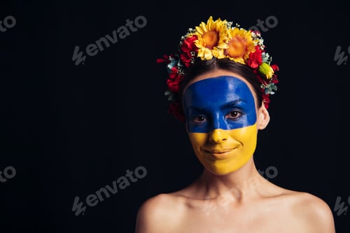 Preview: naked young woman in floral wreath with painted Ukrainian flag on skin smiling isolated on black