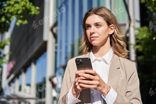 Preview: Portrait of stylish businesswoman in corporate outfit, holding smartphone, standing on street and