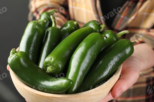 Preview: Woman with ripe green jalapeno peppers on black background, closeup
