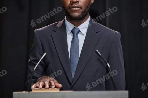 Preview: Male Politician in Suit Holding Hand on Book Taking Oath while Standing at Pulpit Indoors