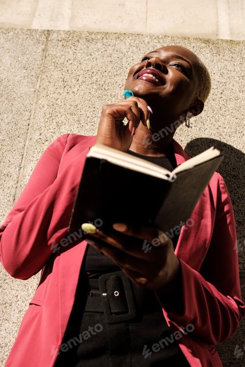 Preview: Smiling businesswoman reading notes in her notebook and thinking outdoors